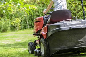 Image is a person on a riding lawn mower doing yard work.