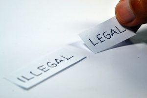 Image is two slips of paper with the words "illegal" and "legal" written on them, being placed next to each other.