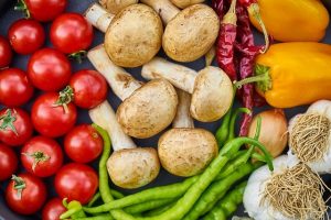 Image is a close up of a bunch of food, such as tomatoes, mushrooms, peppers, green beans, and garlic.